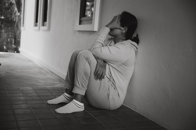 Schizophrenia with lonely and sad in mental health depression concept Depressed woman sitting against floor at home with dark room feeling miserable Women are depressed fearful and unhappy