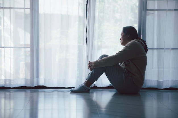 Schizophrenia with lonely and sad in mental health depression concept Depressed woman sitting against floor at home with dark room feeling miserable Women are depressed fearful and unhappy