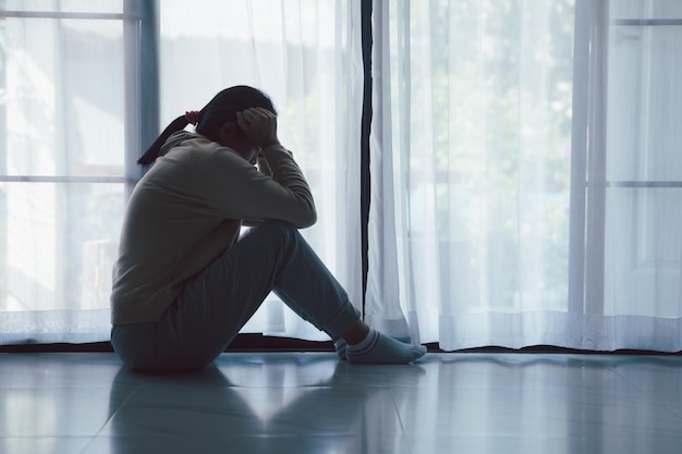 Schizophrenia with lonely and sad in mental health depression concept Depressed woman sitting against floor at home with dark room feeling miserable Women are depressed fearful and unhappy