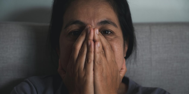 Schizophrenia with lonely and sad in mental health depression concept Depressed woman sitting against on the sofa at home with dark room feeling miserable Women are depressed fearful and unhappy