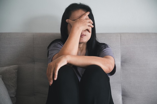 Schizophrenia with lonely and sad in mental health depression concept Depressed woman sitting against on the sofa at home with dark room feeling miserable Women are depressed fearful and unhappy