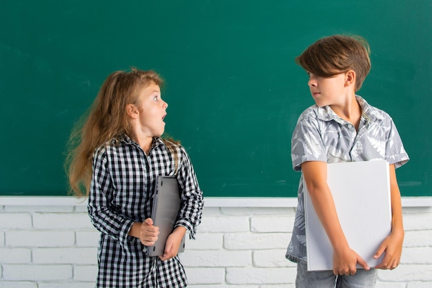 School amazed siblings children hold book with surprising expression against blackboard School kids friends