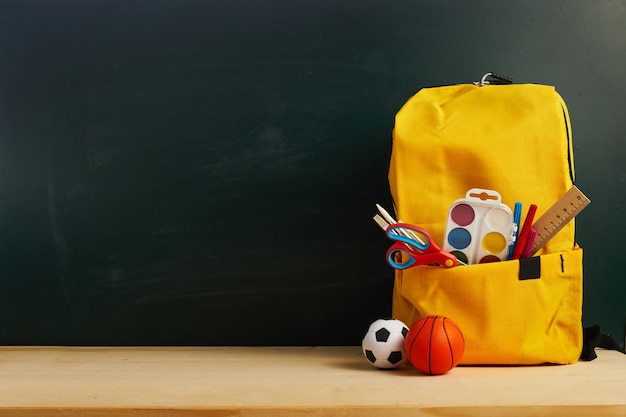 School backpack with colorful school supplies on table