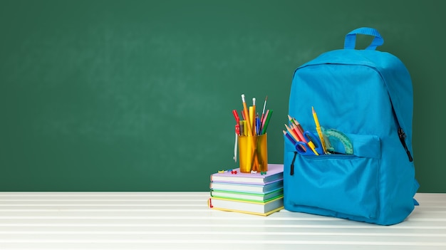 School bag with supplies for school on blackboard background. Copy space for text.