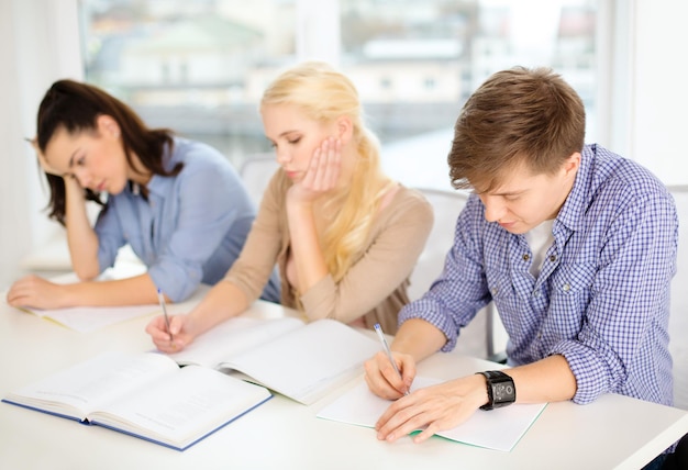 school and education concept - group of tired students with notebooks at school