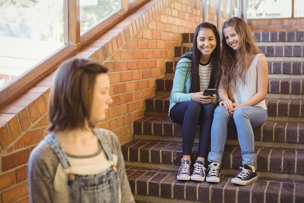 School friends bullying a sad girl in school corridor