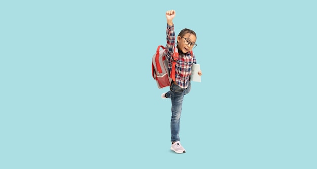 School girl Happy Asian student school kid hand fists like winner with backpack and holding book Full body portrait isolated on pastel plain light blue background with clipping path for design work