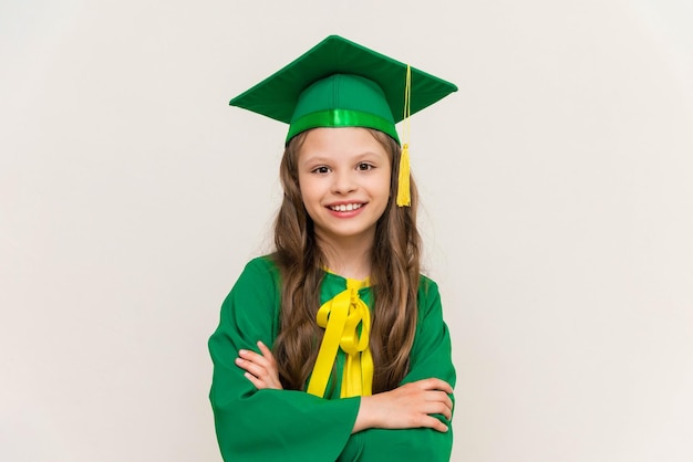 School girl in a master's suit folded her arms on her chest and rejoices at the graduation The student rejoices in the master hat Children's education White isolated background at the graduation