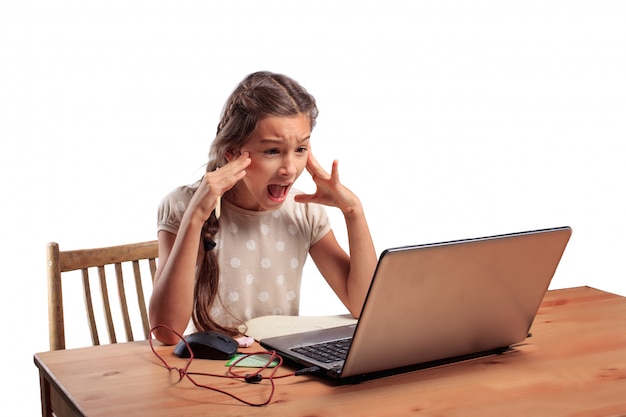 School girl sitting at the table with a laptop with an expressive emotional face taking a hard exam online, bad scores on test and homeschooling concept