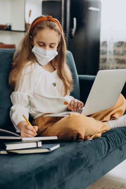 School girl studying at home wearing mask, distant learning