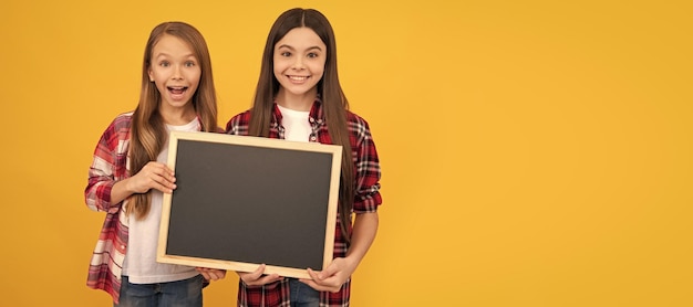 School girls friends happy children in casual checkered hold school blackboard for copy space