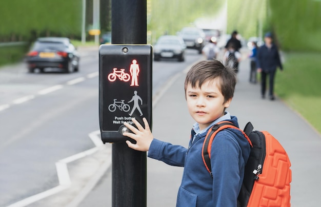 School kid pressing a button at traffic lights on pedestrian crossing on way to school Child boy with backpack using traffic signal controlled pedestrian facilities for crossing road