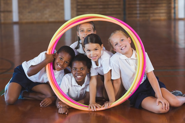 School kids looking through hula hoop in basketball court