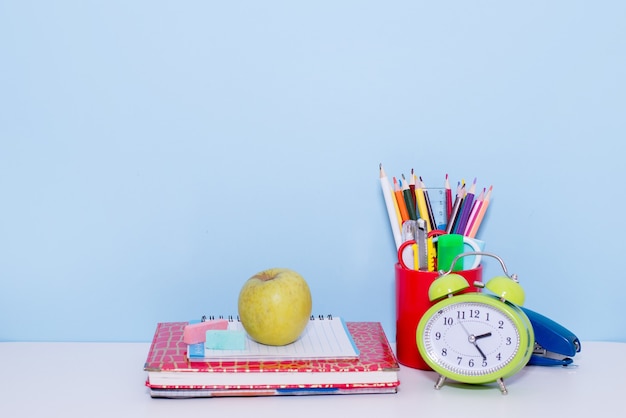 School and office supplies with green apple and alarm clock on blue scene, back to school