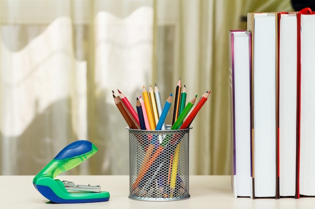 School supplies. Books, colour pencils, stapler on wooden table. Back to school concept.