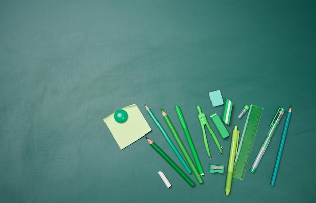 School supplies on empty green chalk board top view