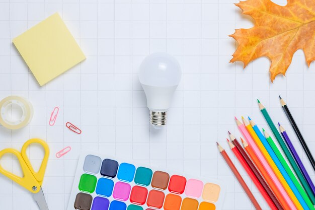 School supplies and a light bulb on a white checkered paper background Back to school