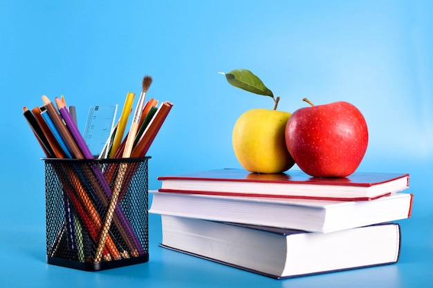  School supplies pencils, pens, ruler, brush, books and apple on blue 