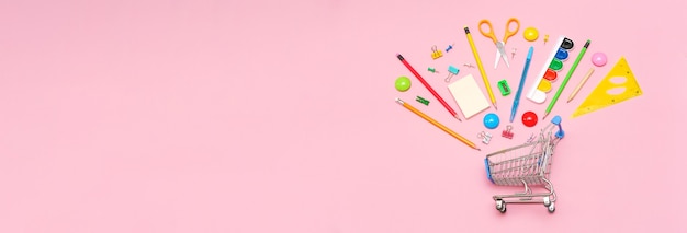 School supplies on pink background in shopping cart view from above copy space office for the studen...