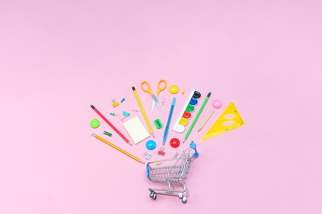 School supplies on pink background in shopping cart view from above copy space office