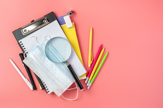 School supplies and protective masks on a pink background. Top view. Back to school.