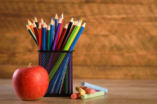 School supplies on a warm, beautiful wooden background. Colored children's pencils in a locker black holder for stationery.