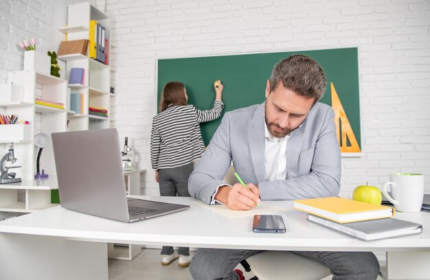 School teacher in classroom with selective focus of kid at blackboard