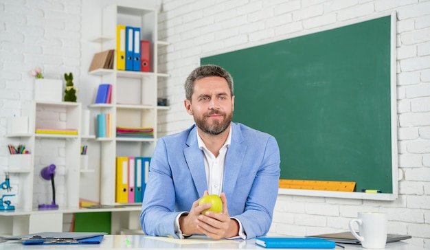 School teacher hold apple in classroom at blackboard