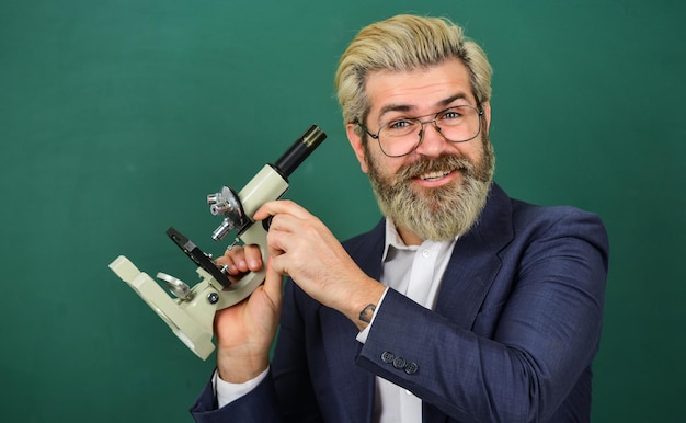 Photo school teacher looking microscope. scientific research. fascinating research. teacher with microscope. man hipster classroom chalkboard background. biological research. facilitate academic progress.