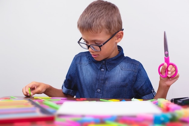 Schoolboy in a blue shirt sitting at the table. Boy with glasses. Concept back to school