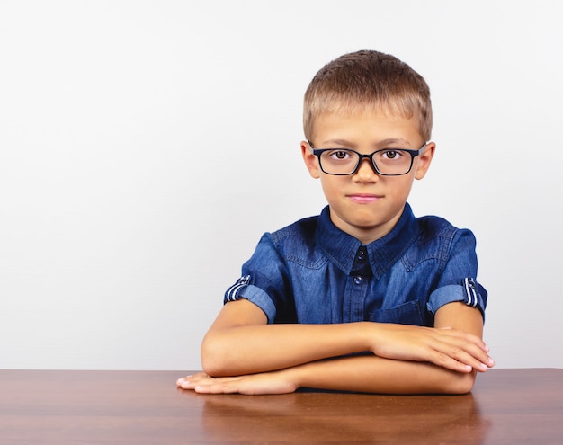 Schoolboy in a blue shirt sitting at the table. Boy with glasses