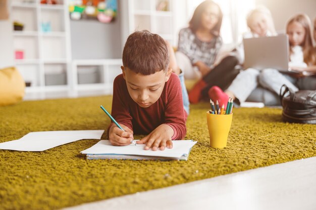 Schoolboy holding a pencil and drawing on paper on the floor