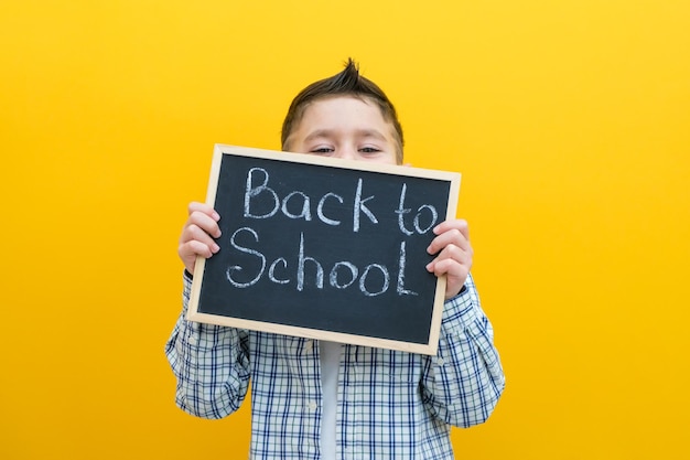 Schoolboy holding a tablet in his hands with the inscription Back to school on a yellow background