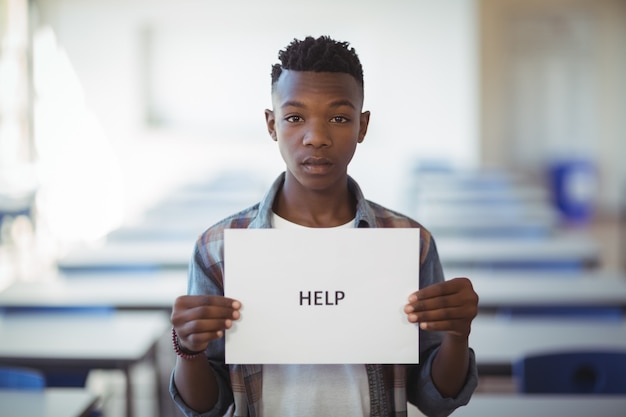 Schoolboy holding white paper with text sign in classroom