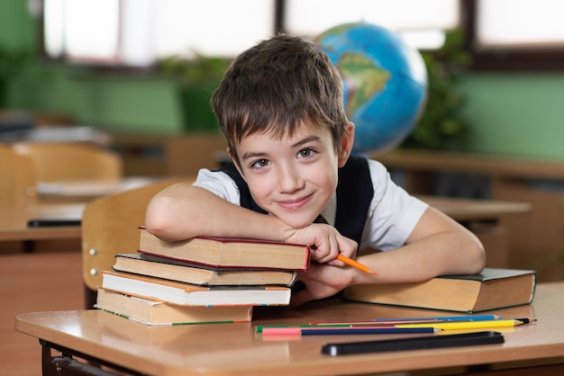 A schoolboy is sitting at a desk in an empty classroom and is writing something in a notebook