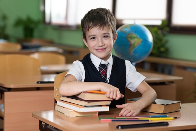 A schoolboy is sitting at a desk in an empty classroom and is writing something in a notebook