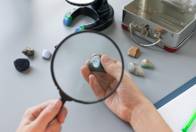 Schoolboy looking at semiprecious stones through magnifying glass at school lesson Education