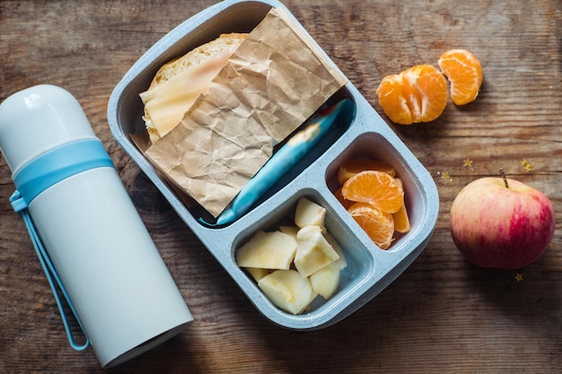 Schoolboy lunch box with thermos on wooden backgroundappletangerinesandwich in lunchbox and water bottle