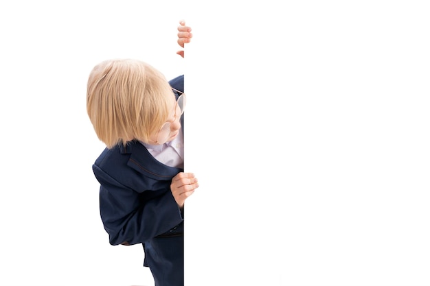 Schoolboy peeking out from behind an empty blank Blond boy in school uniform with blank white poster board peeking Copy space