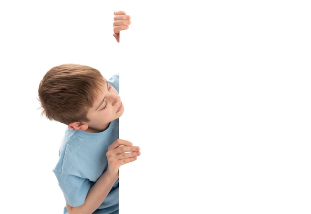 Schoolboy peeks out from behind an empty whiteboard with place for your text Isolated on white background Boy with an empty poster