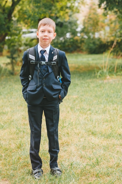 A schoolboy in a school uniform and a backpack stands on the street Boy in school uniform back to school concept and no desire to study