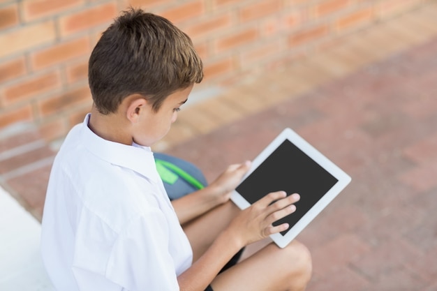 Schoolboy sitting in corridor and using digital tablet