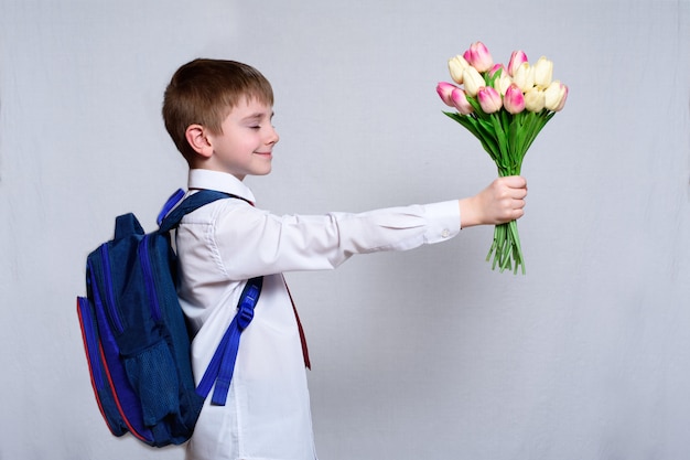 Schoolboy with a school bag gives a bouquet of tulips as gift for mothers day