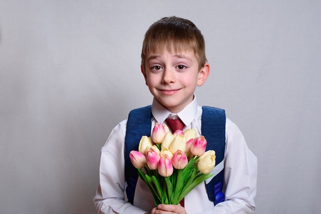 Schoolboy with a school bag holding a bouquet of tulips