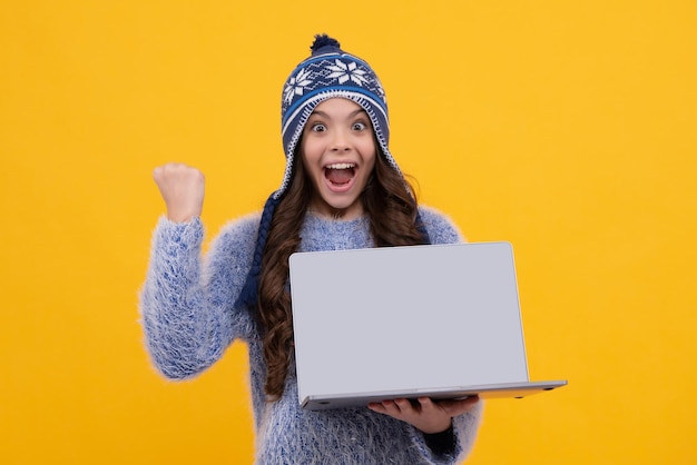 Schoolgirl child student in warn hat hold laptop isolated yellow background Learning and knowledge