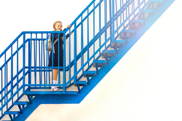 Schoolgirl climbs the stairs Concept  school days  start date next stage career ladder the beginning of the way girl in a uniform with a backpack Girl go up a step up the stairs