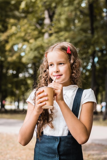 Schoolgirl drinking from an ecofriendly cup and straw in the park Vertical view