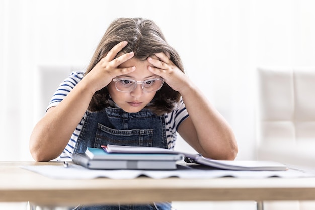 Schoolgirl in glasses tries to comprehend study materials holding her head by both hands