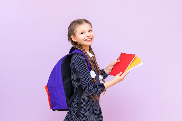 A schoolgirl holding a backpack holds notebooks on a pink isolated background Preparation for the school year