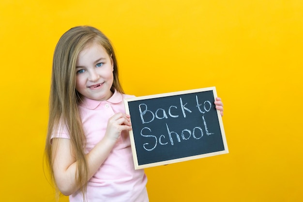 Schoolgirl holding a tablet in her hands with the inscription Back to school on a yellow background